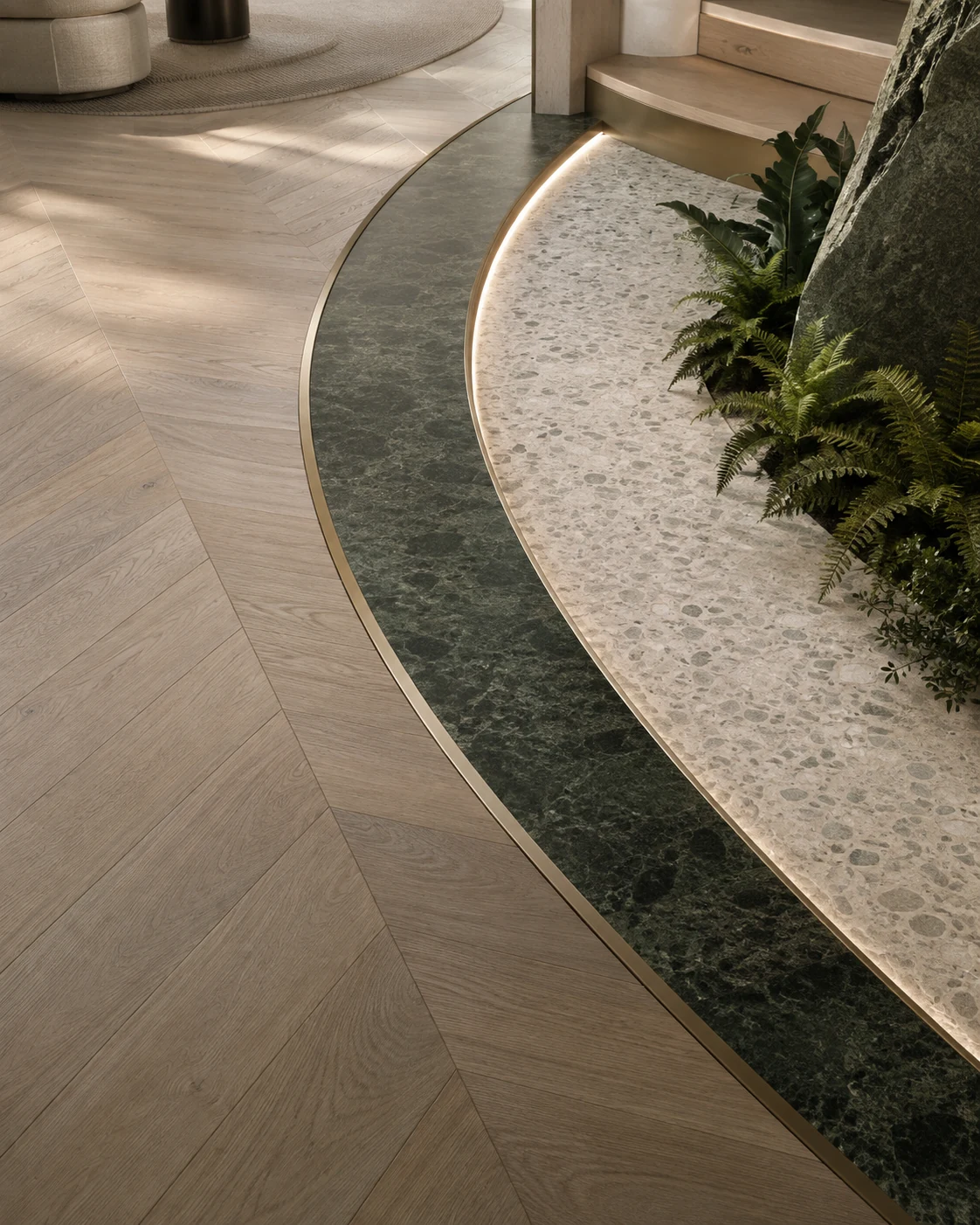 Curved transition between chevron oak, green stone and terrazzo with precision brass profiles