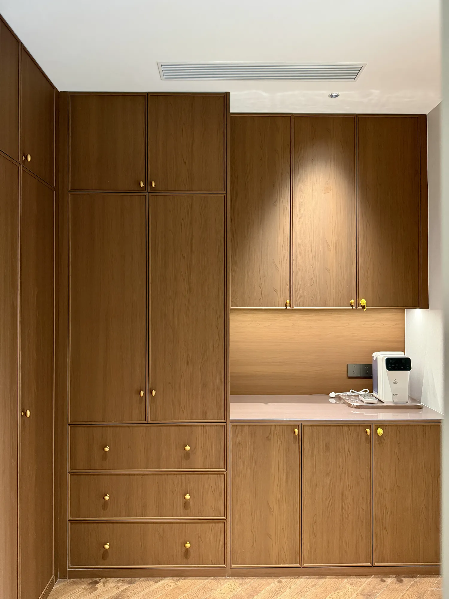 Compact fitted coffee station with warm timber cabinetry and lit worktop