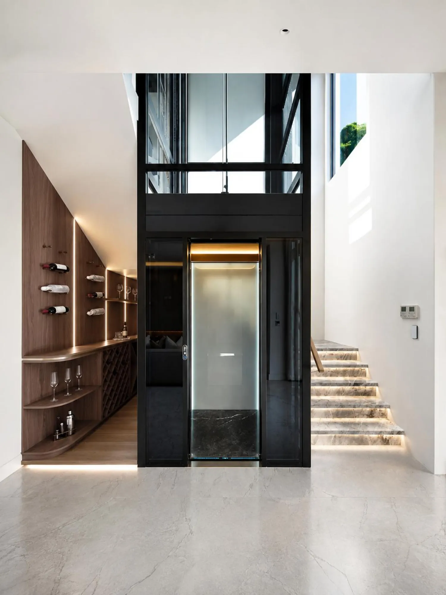 Double-height stair hall with integrated walnut wine wall and glass lift enclosure