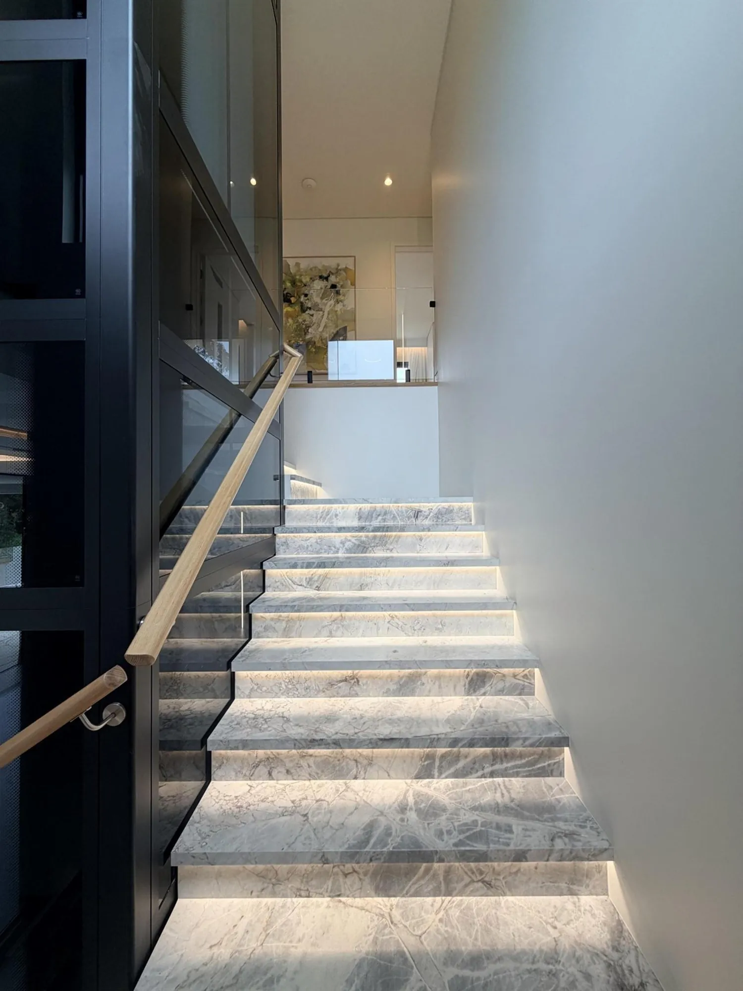 Illuminated stone staircase beside fitted timber wine storage