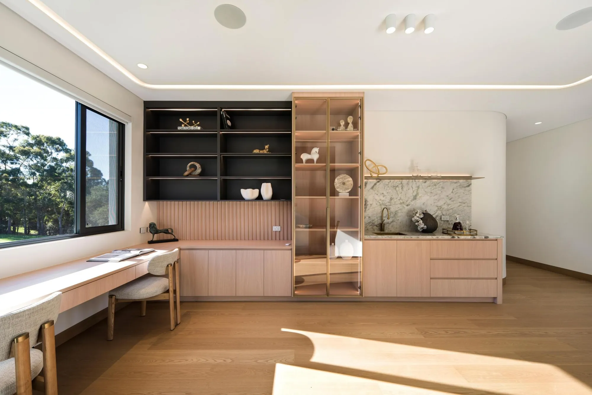 Home study with pale timber desk, black shelving and glass-front display cabinetry