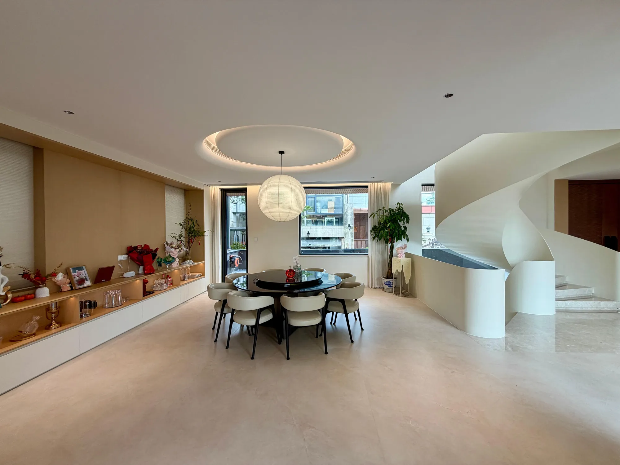 Round dining area with paper pendant, fitted sideboard and curved staircase