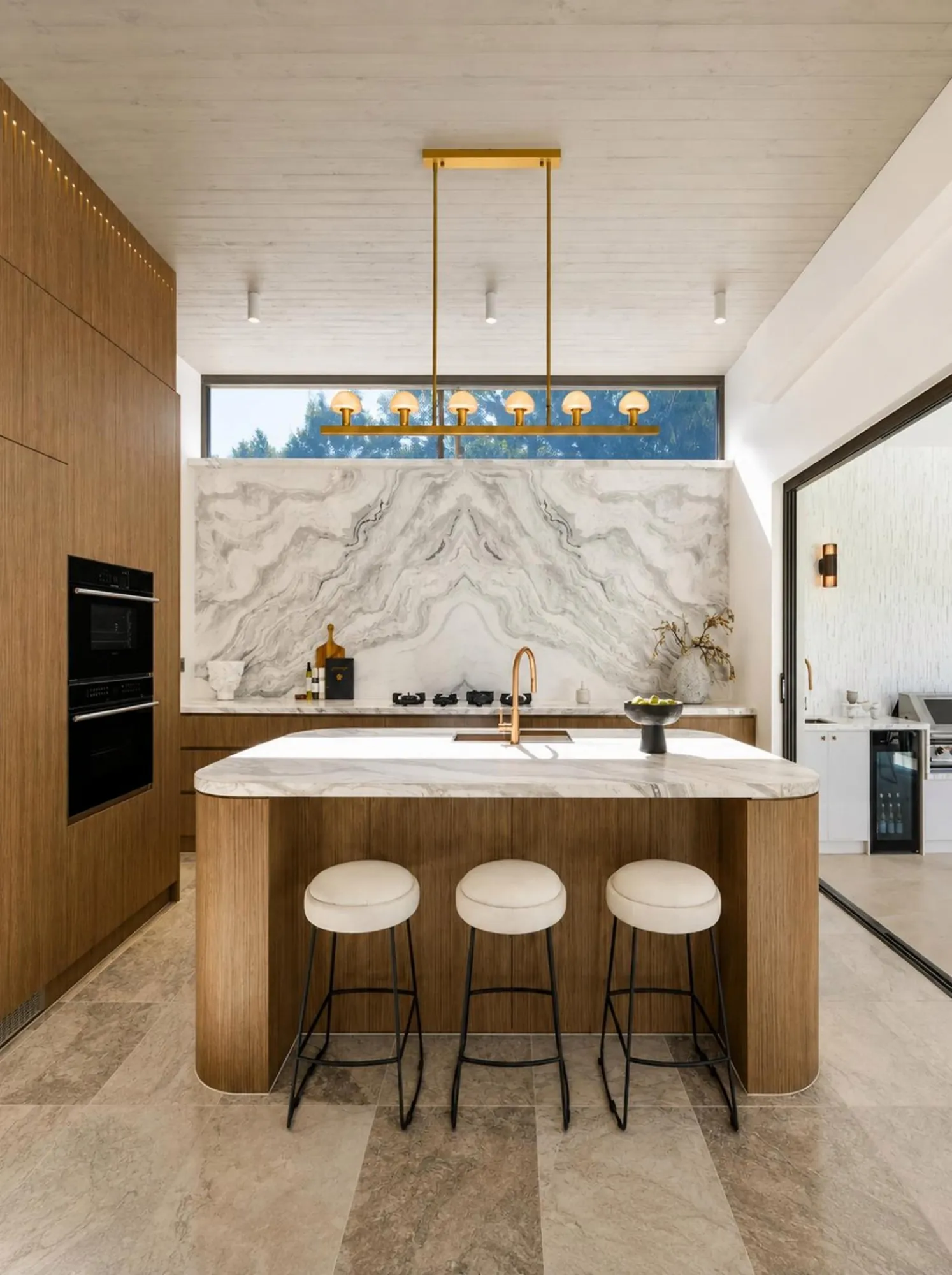 Bright kitchen with marble island, warm timber base and slim pendant light