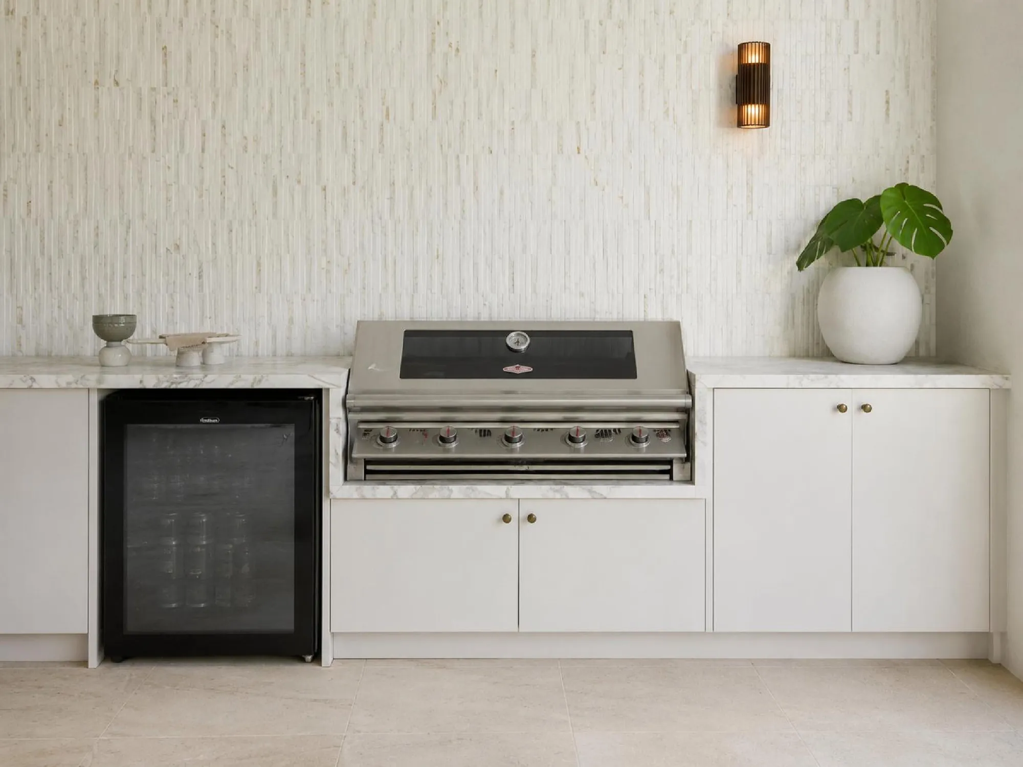 Wide covered outdoor kitchen with fitted white cabinets, barbecue and garden connection