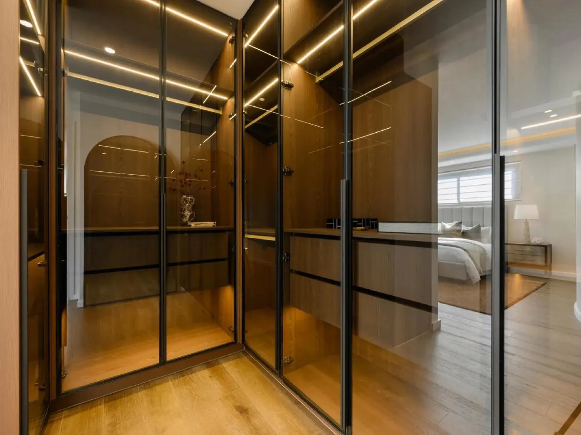 Wide walk-in wardrobe with slim black glass frames and walnut interiors