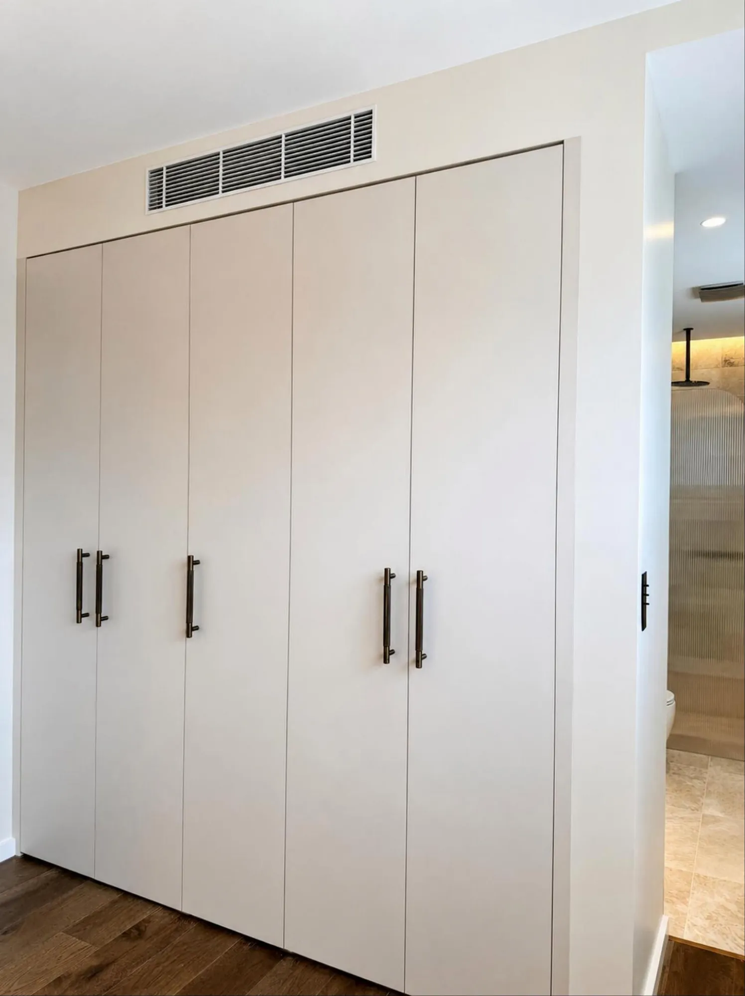 Bedroom with a pale full-height fitted wardrobe and aligned ventilation grille