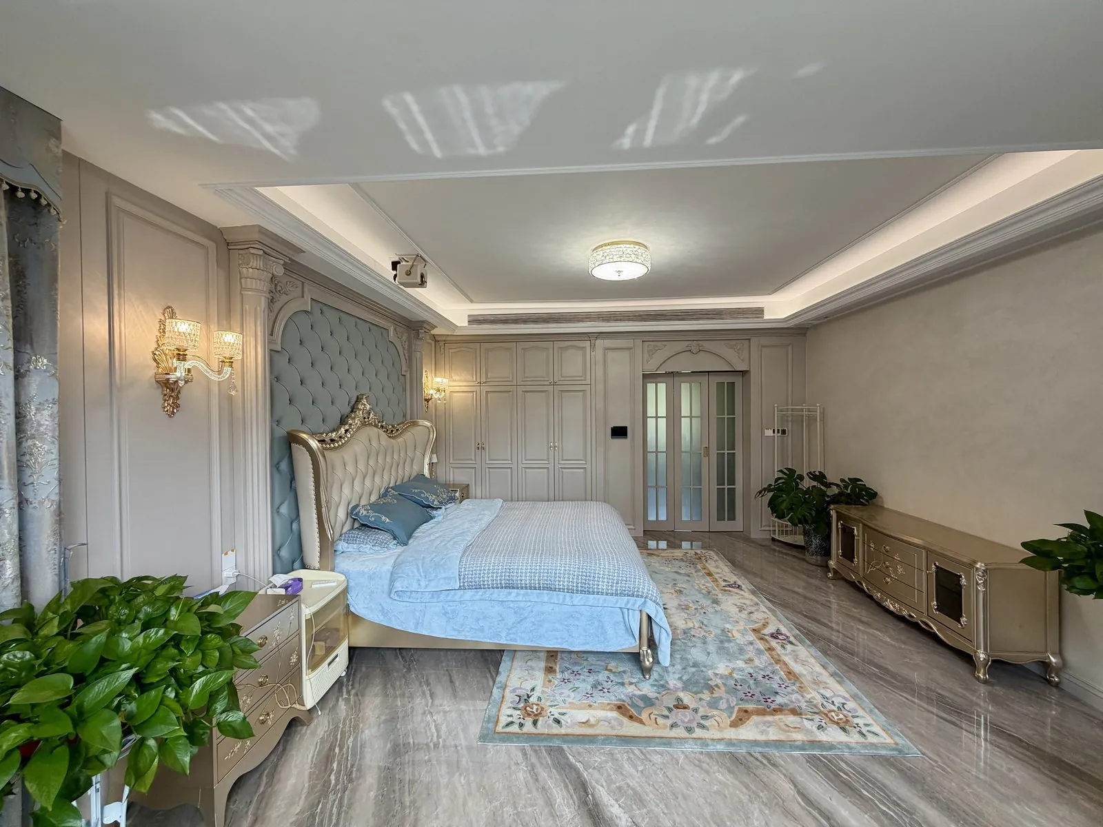 Main bedroom with blue upholstered bed, painted hardwood panels and French doors